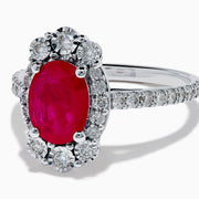 The Ruby Royale 14K White Gold Ruby and Diamond Ring showcases an oval red ruby center, a halo of round white diamonds, and additional diamonds along the band.