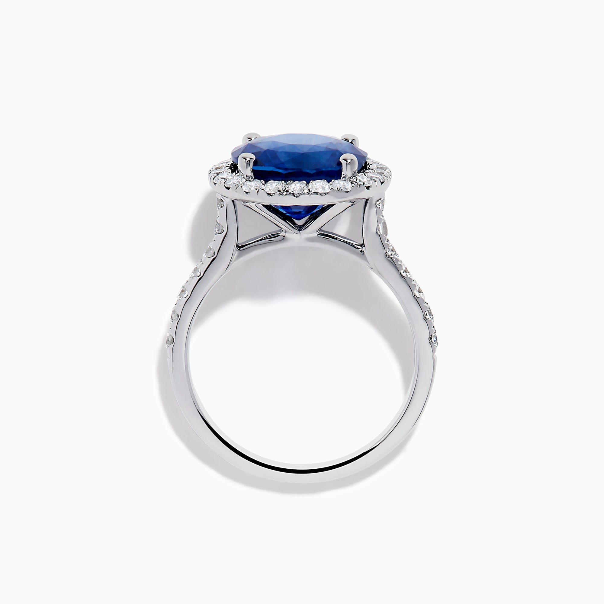 The Royale Blue 18K White Gold Blue Sapphire and Diamond Ring features a striking round blue sapphire center, encircled by a halo of sparkling diamonds, displayed against a white background.