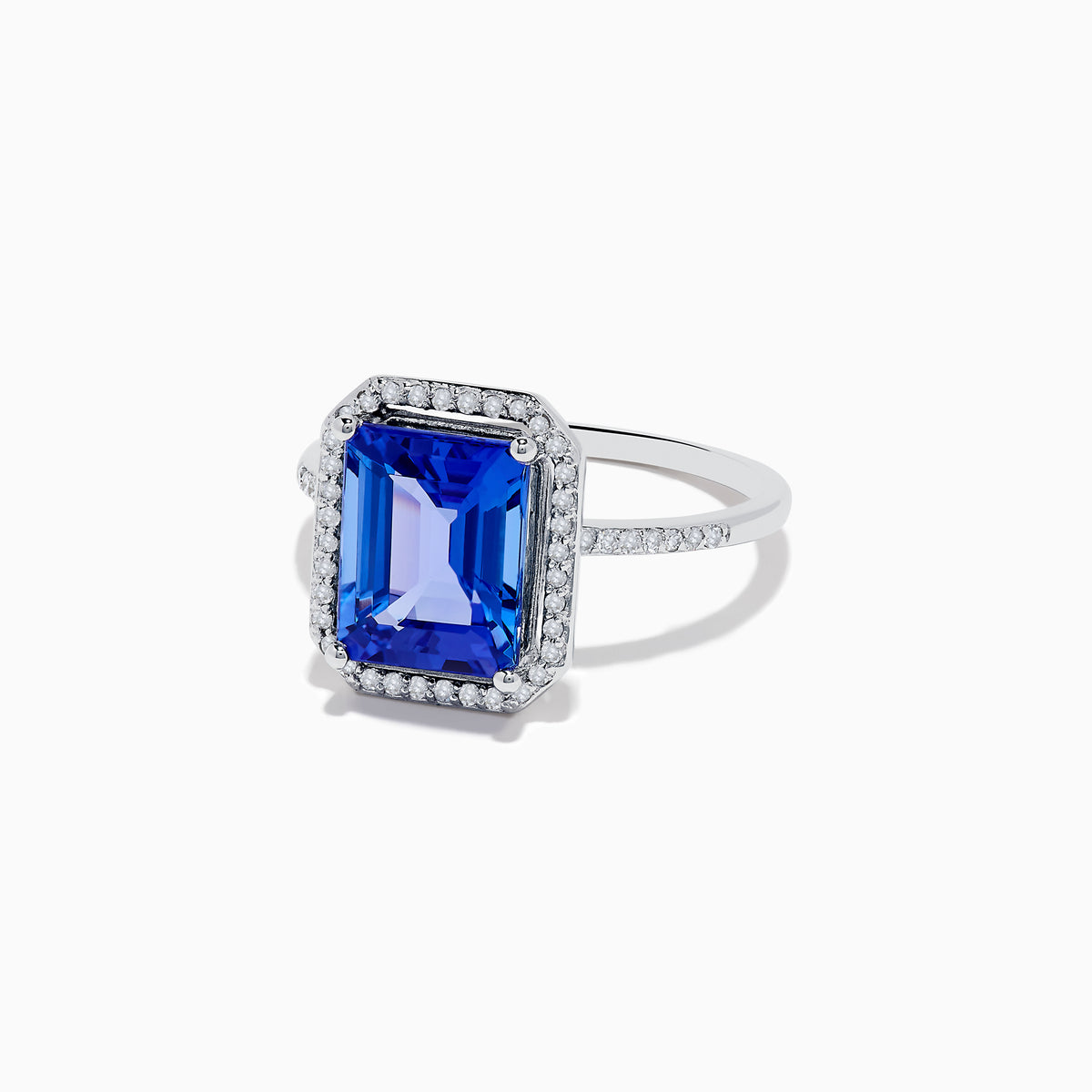The Nahla Siri 14K White Gold Tanzanite and Diamond Ring features a large emerald-cut blue tanzanite, haloed by small white diamonds with additional diamonds set along the band.