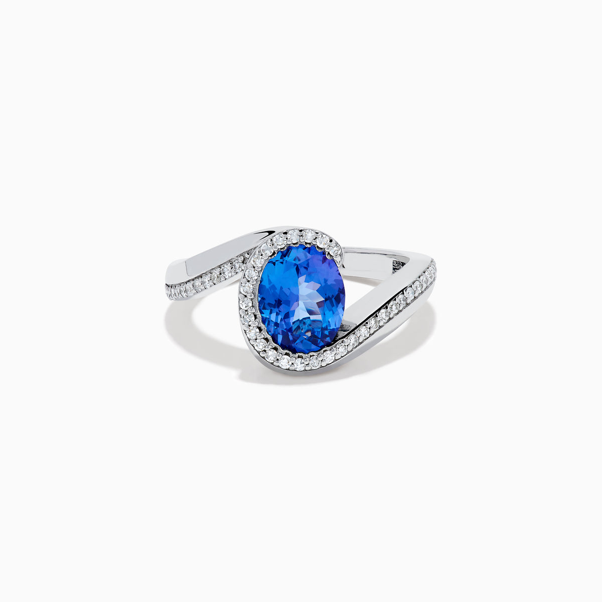 The 14K White Gold Tanzanite and Diamond Oval Swirl Ring features an oval tanzanite center stone accented by sparkling diamonds, all set on a modern, asymmetrical swirl band.