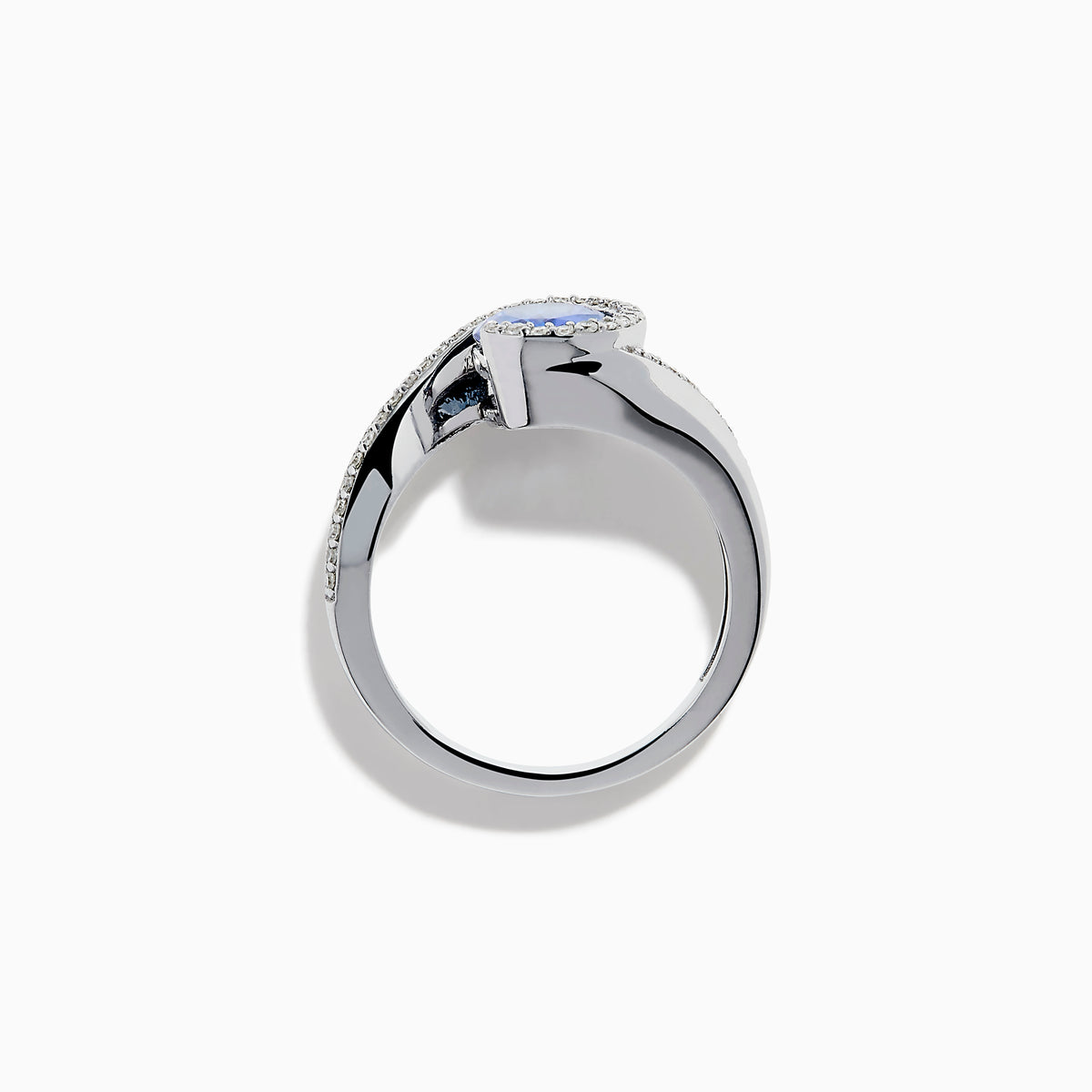 The 14K White Gold Tanzanite and Diamond Oval Swirl Ring features an oval tanzanite center stone accented by sparkling diamonds, all set on a modern, asymmetrical swirl band.