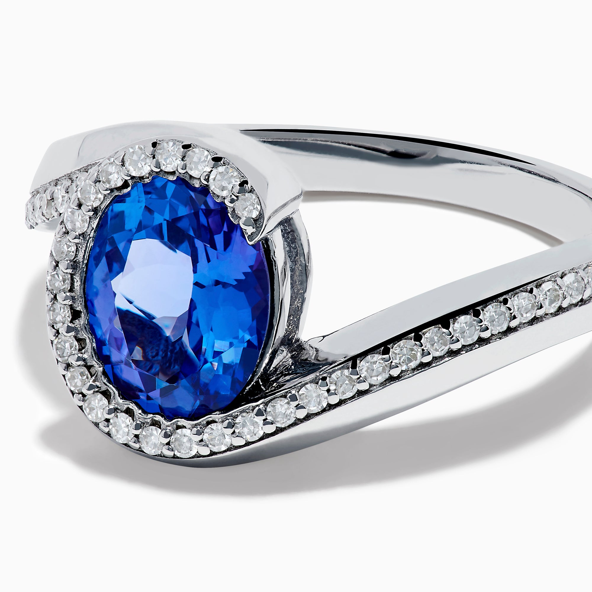 The 14K White Gold Tanzanite and Diamond Oval Swirl Ring features an oval tanzanite center stone accented by sparkling diamonds, all set on a modern, asymmetrical swirl band.
