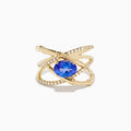 The Nahla 14K Yellow Gold Tanzanite and Diamond Criss Cross Ring features an oval tanzanite centerpiece and sparkling diamond crisscross bands, all set against a white background.