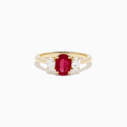 The 14K Yellow Gold Ruby and Diamond Three-Stone Ring showcases a striking oval ruby center with two oval white diamonds, set in yellow gold and displayed on a white background.