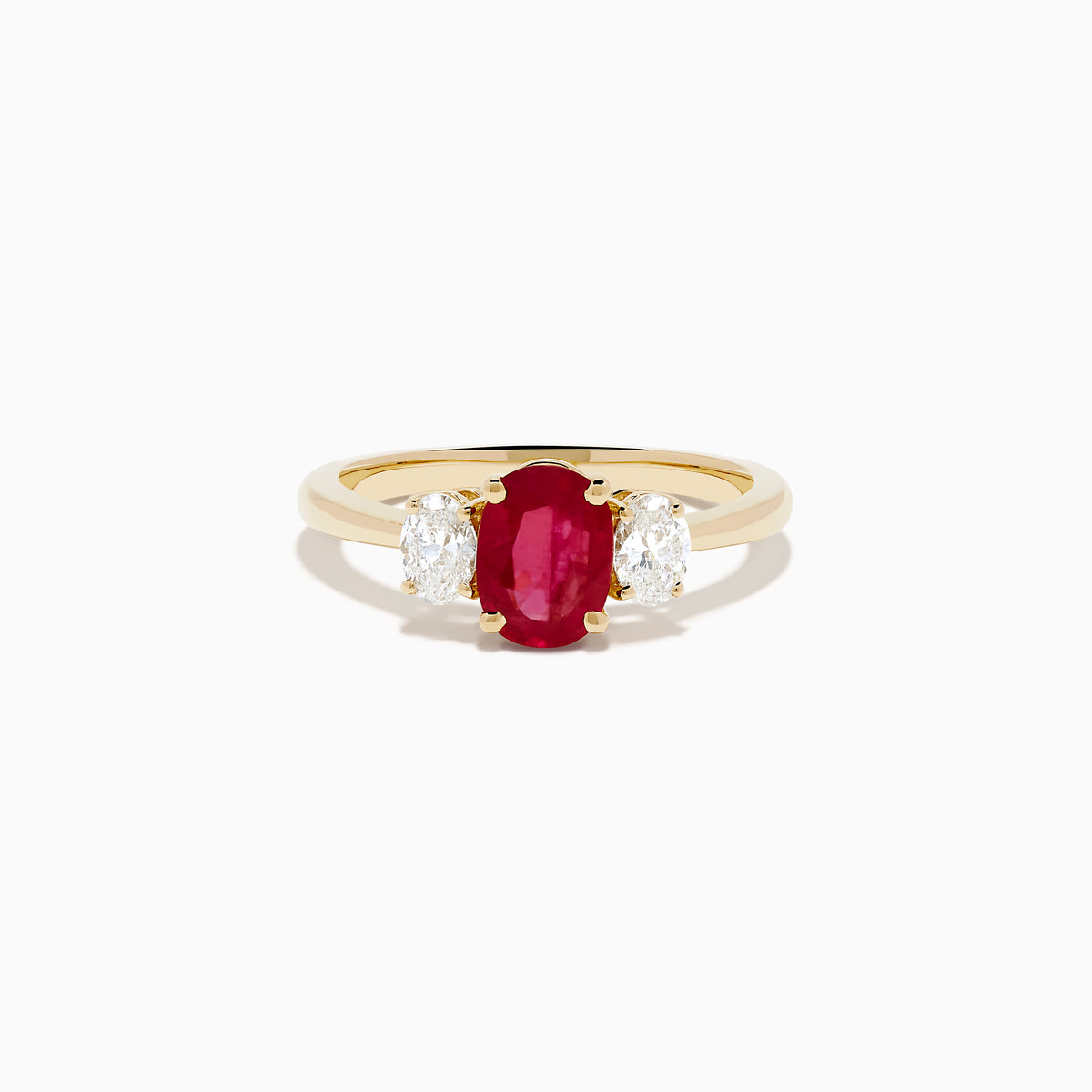 The 14K Yellow Gold Ruby and Diamond Three-Stone Ring showcases a striking oval ruby center with two oval white diamonds, set in yellow gold and displayed on a white background.