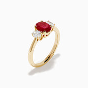 The 14K Yellow Gold Ruby and Diamond Three-Stone Ring showcases a striking oval ruby center with two oval white diamonds, set in yellow gold and displayed on a white background.