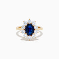 The 14K Yellow Gold Natural Blue Sapphire and Diamond Lady Di Ring features an oval sapphire center, haloed by round white diamonds, shown on a white background.