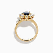 The 14K Yellow Gold Natural Blue Sapphire and Diamond Lady Di Ring features an oval sapphire center, haloed by round white diamonds, shown on a white background.