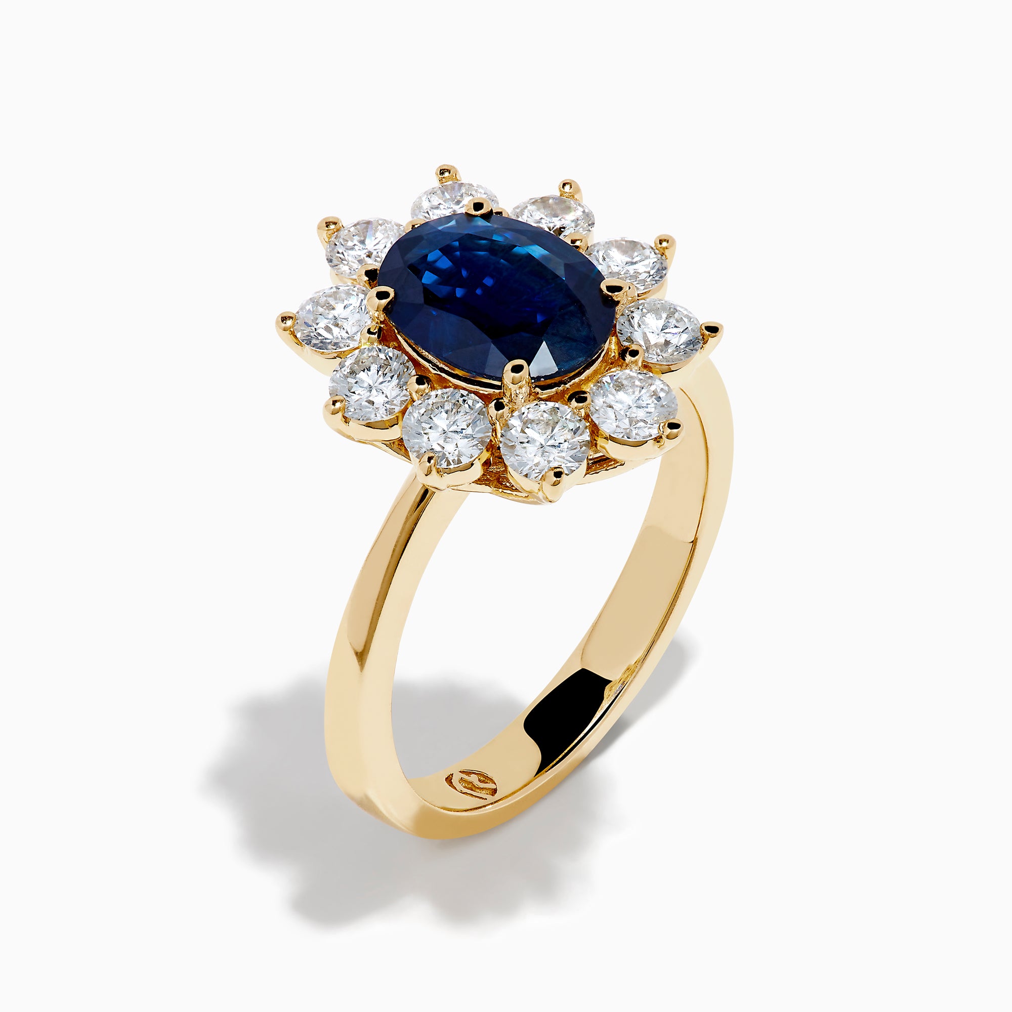 The 14K Yellow Gold Natural Blue Sapphire and Diamond Lady Di Ring features an oval sapphire center, haloed by round white diamonds, shown on a white background.