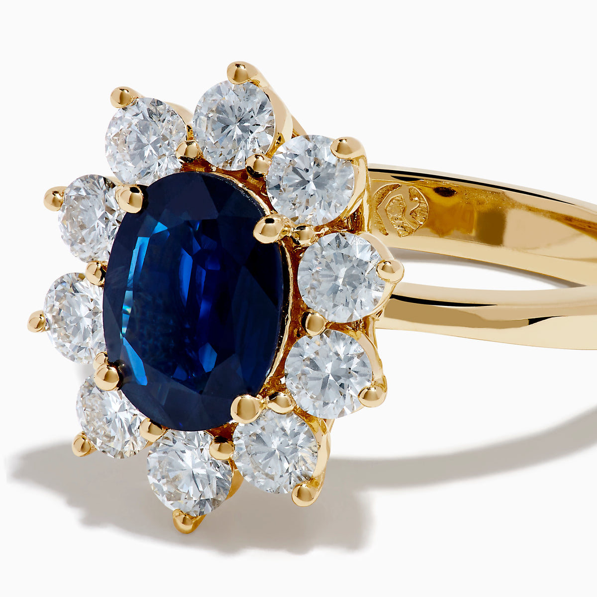 The 14K Yellow Gold Natural Blue Sapphire and Diamond Lady Di Ring features an oval sapphire center, haloed by round white diamonds, shown on a white background.