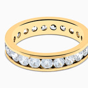 The 14K Yellow Gold Channel Set Diamond Eternity Band, 2.00 TCW, features round white diamonds encircling the band and is beautifully showcased against a plain white background.
