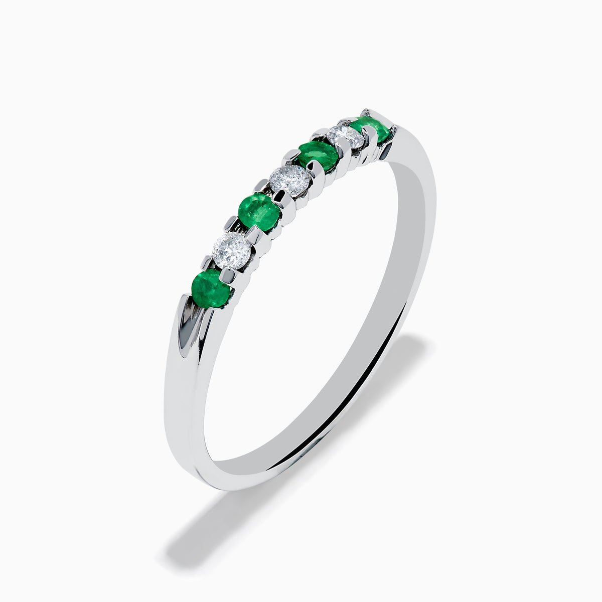 The 14K White Gold 7-Stone Emerald & Diamond Band, 0.25 TCW, showcases alternating round emeralds and diamonds set in a row along the band, displayed on a plain white background.