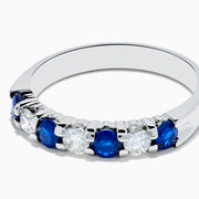 The 14K White Gold 7-Stone Blue Sapphire & Diamond Band, 0.65 TCW, features alternating round blue sapphires and sparkling white diamonds in a row on the band, shown against a white background.