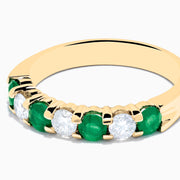 The 14K Yellow Gold 7-Stone Emerald & Diamond Band, 1.00 TCW, features alternating round white diamonds and vibrant emeralds set in a row, shown against a plain white background.