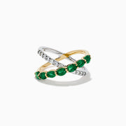 The 14K Two Tone Gold Emerald and Diamond Criss Cross Ring features intertwined yellow gold with green emeralds and white gold with clear round diamonds for a striking, modern look.