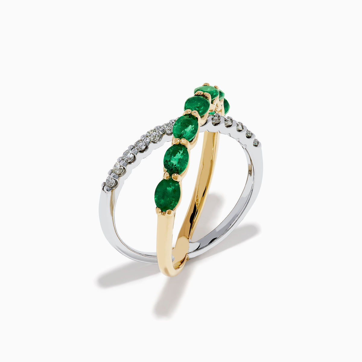 The 14K Two Tone Gold Emerald and Diamond Criss Cross Ring features intertwined yellow gold with green emeralds and white gold with clear round diamonds for a striking, modern look.