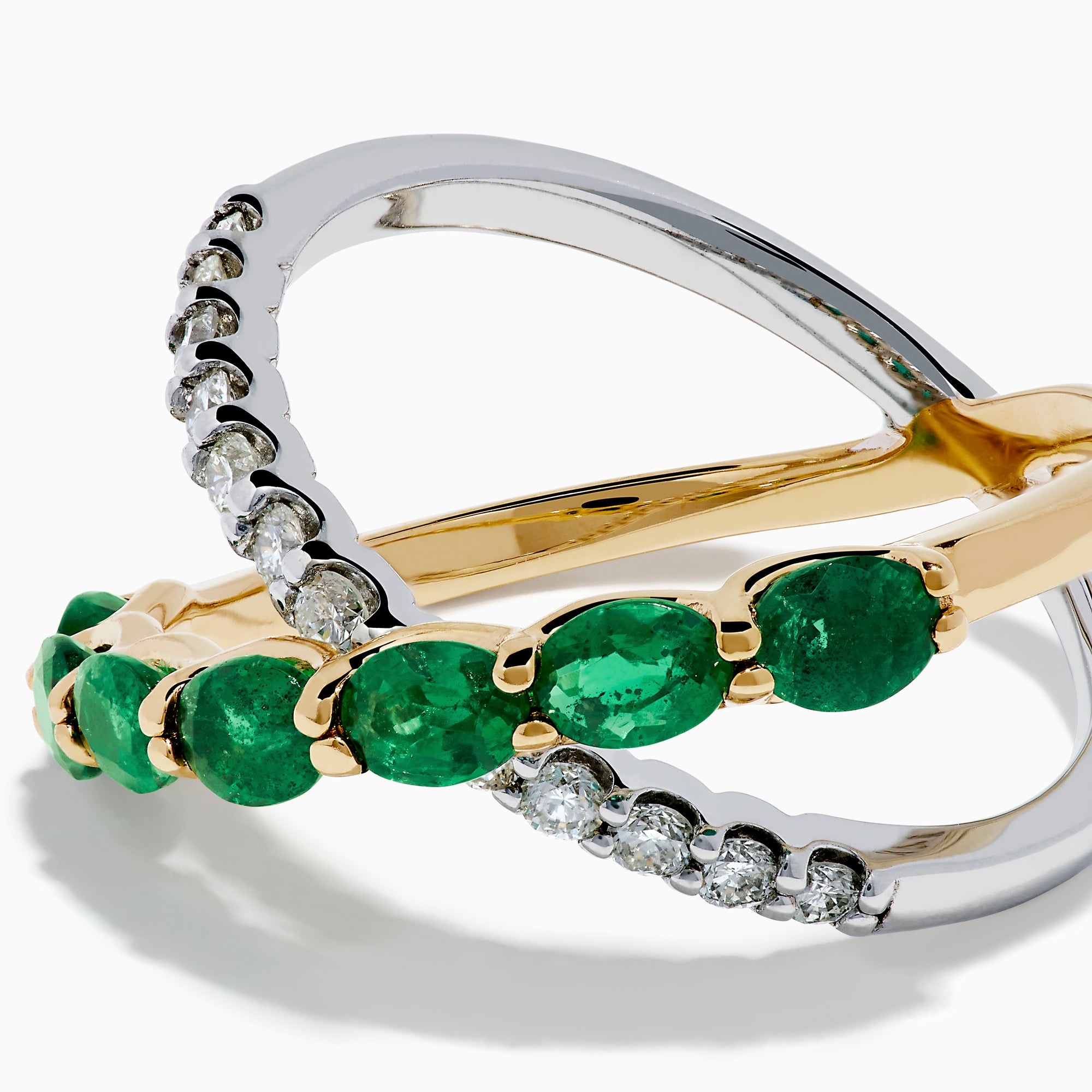 The 14K Two Tone Gold Emerald and Diamond Criss Cross Ring features intertwined yellow gold with green emeralds and white gold with clear round diamonds for a striking, modern look.