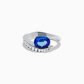 The Nahla 14K White Gold Floating Tanzanite and Diamond Ring showcases an oval blue tanzanite center with a curved band of round diamonds, all set in white gold and displayed on a white background.
