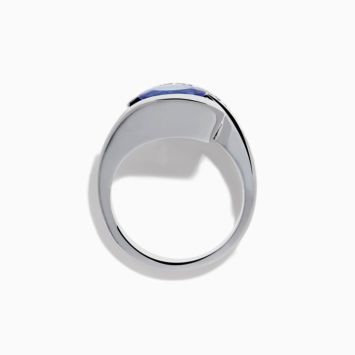 The Nahla 14K White Gold Floating Tanzanite and Diamond Ring showcases an oval blue tanzanite center with a curved band of round diamonds, all set in white gold and displayed on a white background.