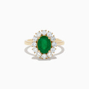 The 14K Yellow Gold Emerald and Diamond Ring showcases an oval emerald center accented by a halo of round white diamonds, displayed against a white background.