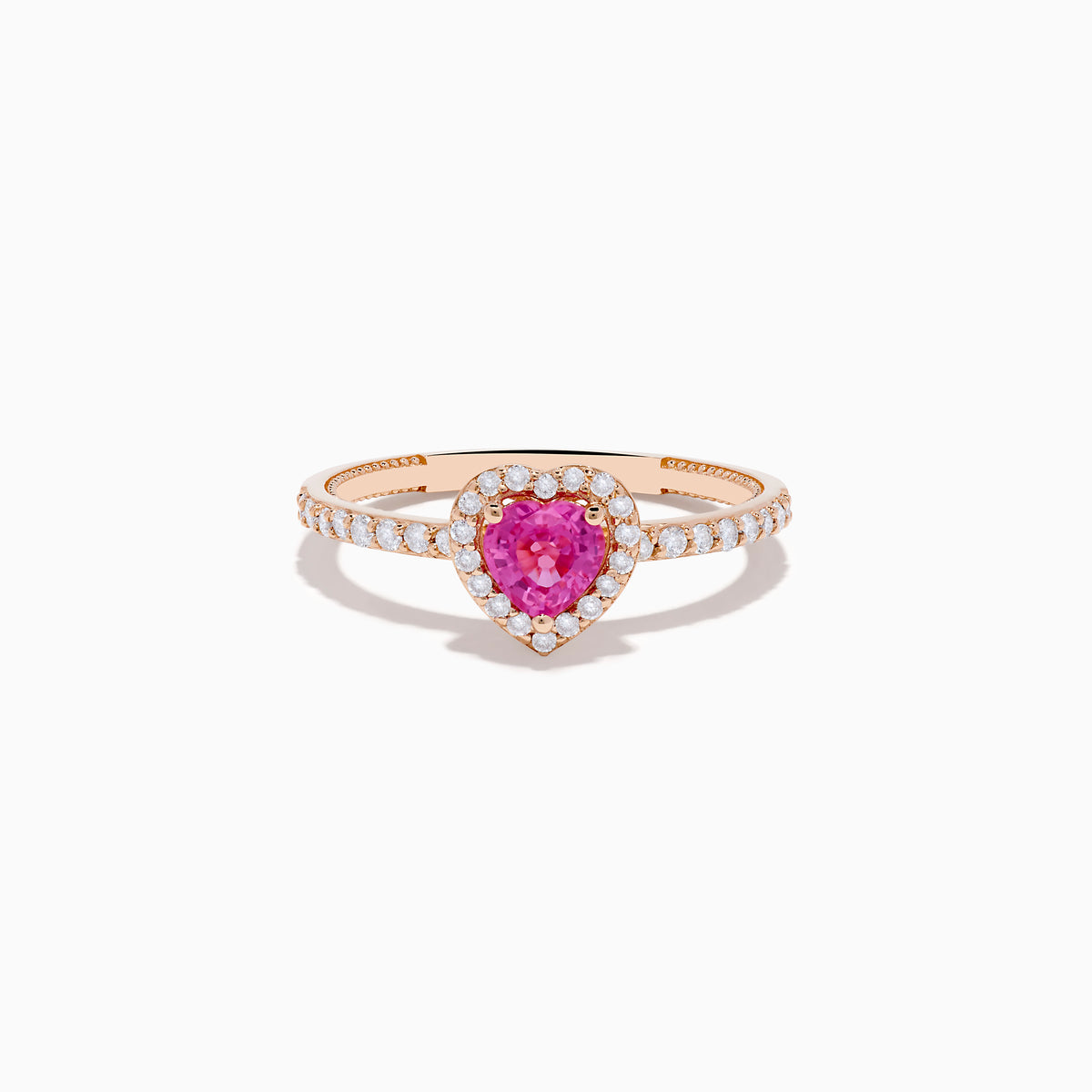 The Novelty 14K Rose Gold Pink Sapphire and Diamond Heart Ring showcases a heart-shaped pink sapphire center, a halo of white diamonds, and extra diamonds accenting the band.