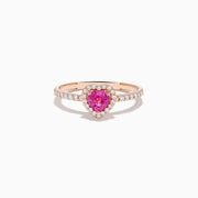 The Novelty 14K Rose Gold Pink Sapphire and Diamond Heart Ring showcases a heart-shaped pink sapphire center, a halo of white diamonds, and extra diamonds accenting the band.