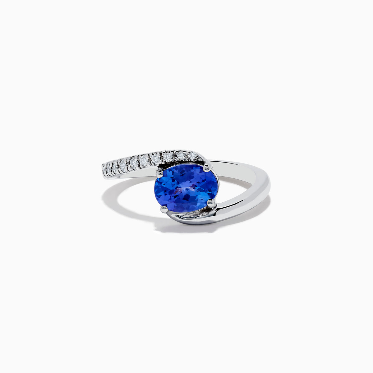 The Nahla Siri 14K White Gold Tanzanite and Diamond Ring features a large oval tanzanite center stone accented by a curved row of small clear diamonds on one side, displayed against a plain white background.