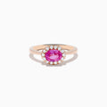 The 14K Rose Gold Pink Sapphire and Diamond Ring showcases an oval pink sapphire center, accented by a halo of round white diamonds, all set against a white background.