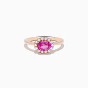 The 14K Rose Gold Pink Sapphire and Diamond Ring showcases an oval pink sapphire center, accented by a halo of round white diamonds, all set against a white background.