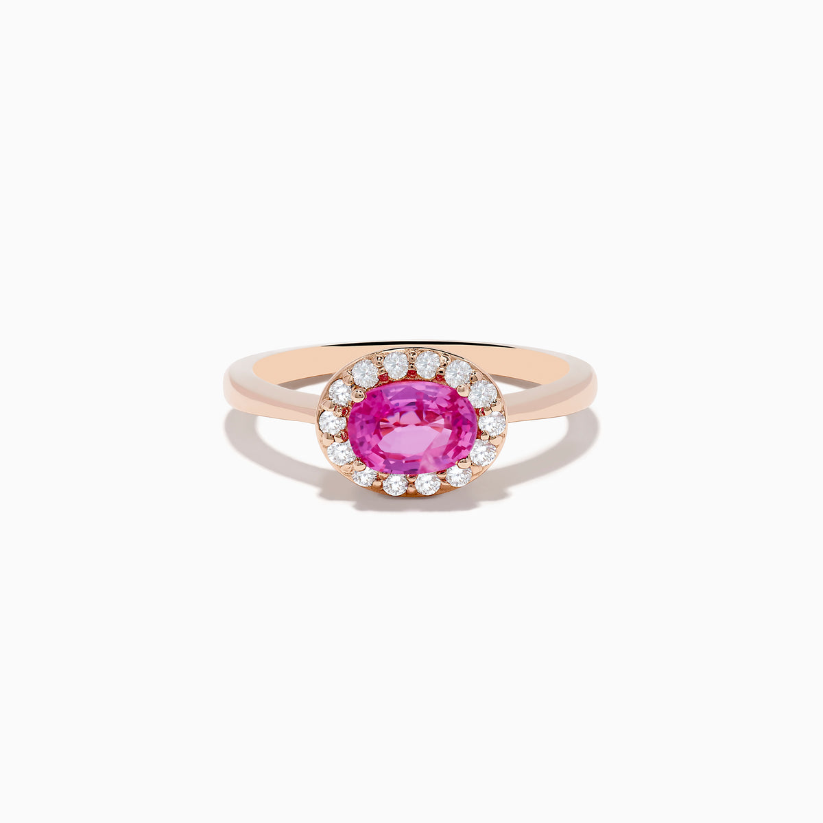 The 14K Rose Gold Pink Sapphire and Diamond Ring showcases an oval pink sapphire center, accented by a halo of round white diamonds, all set against a white background.