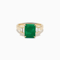 The 14K Yellow Gold Emerald and Diamond Solitaire Ring showcases a vibrant rectangular emerald at its center, accented by two baguette-cut diamonds on each side for a truly elegant look.