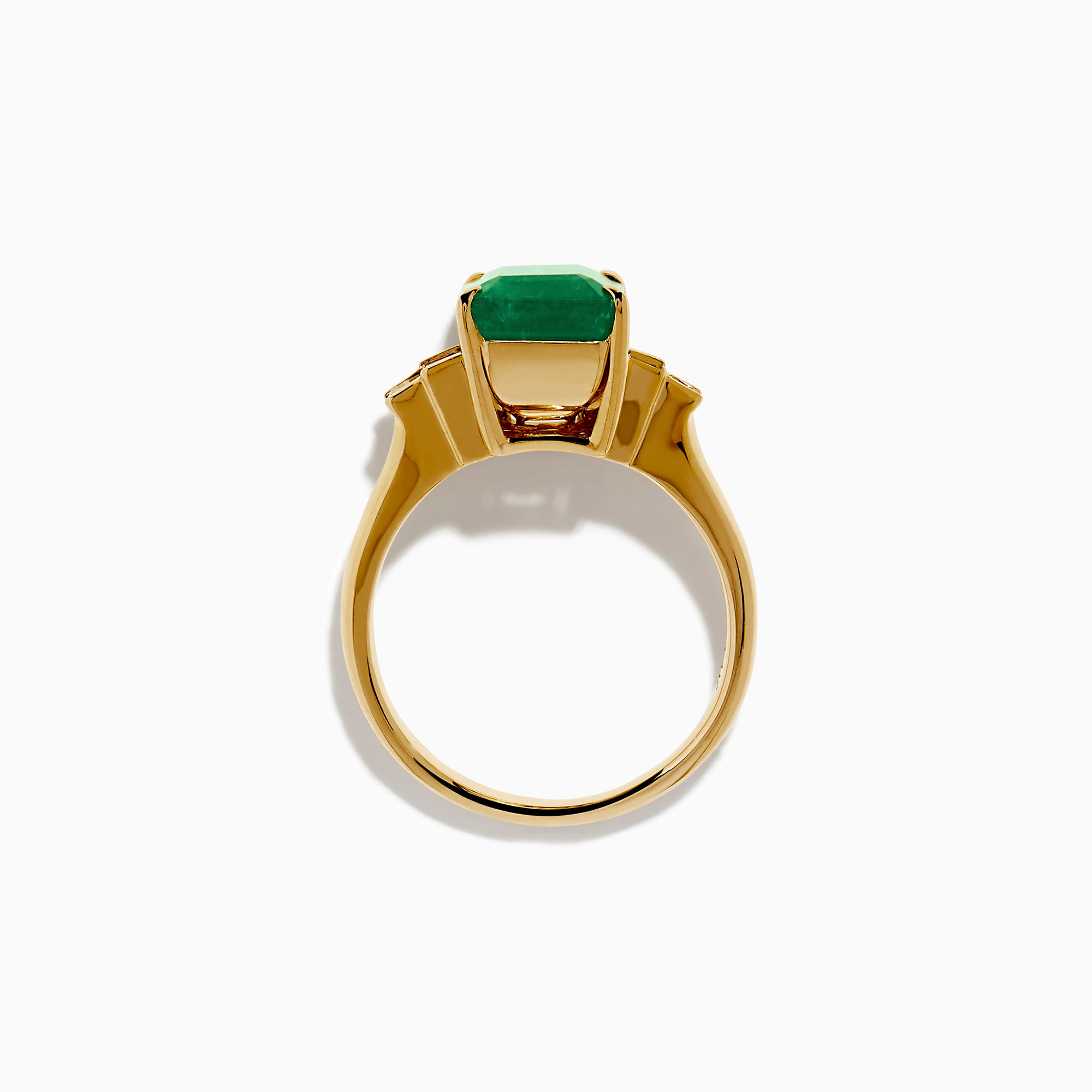 The 14K Yellow Gold Emerald and Diamond Solitaire Ring showcases a vibrant rectangular emerald at its center, accented by two baguette-cut diamonds on each side for a truly elegant look.