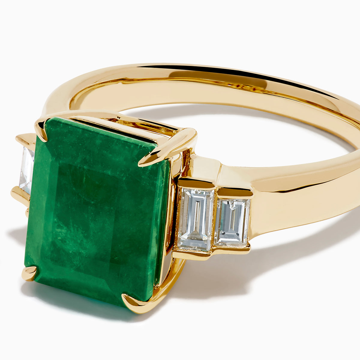 The 14K Yellow Gold Emerald and Diamond Solitaire Ring showcases a vibrant rectangular emerald at its center, accented by two baguette-cut diamonds on each side for a truly elegant look.