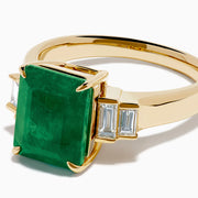 The 14K Yellow Gold Emerald and Diamond Solitaire Ring showcases a vibrant rectangular emerald at its center, accented by two baguette-cut diamonds on each side for a truly elegant look.