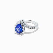 The Nahla Siri 14K White Gold Floating Tanzanite and Diamond Ring features a large pear-shaped blue tanzanite center and a curved band with sparkling round white diamonds on one side, set against a plain white background.