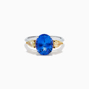 A striking 18K two tone gold ring featuring a large oval blue tanzanite center and two pear-shaped yellow diamonds on each side, displayed against a plain white background.