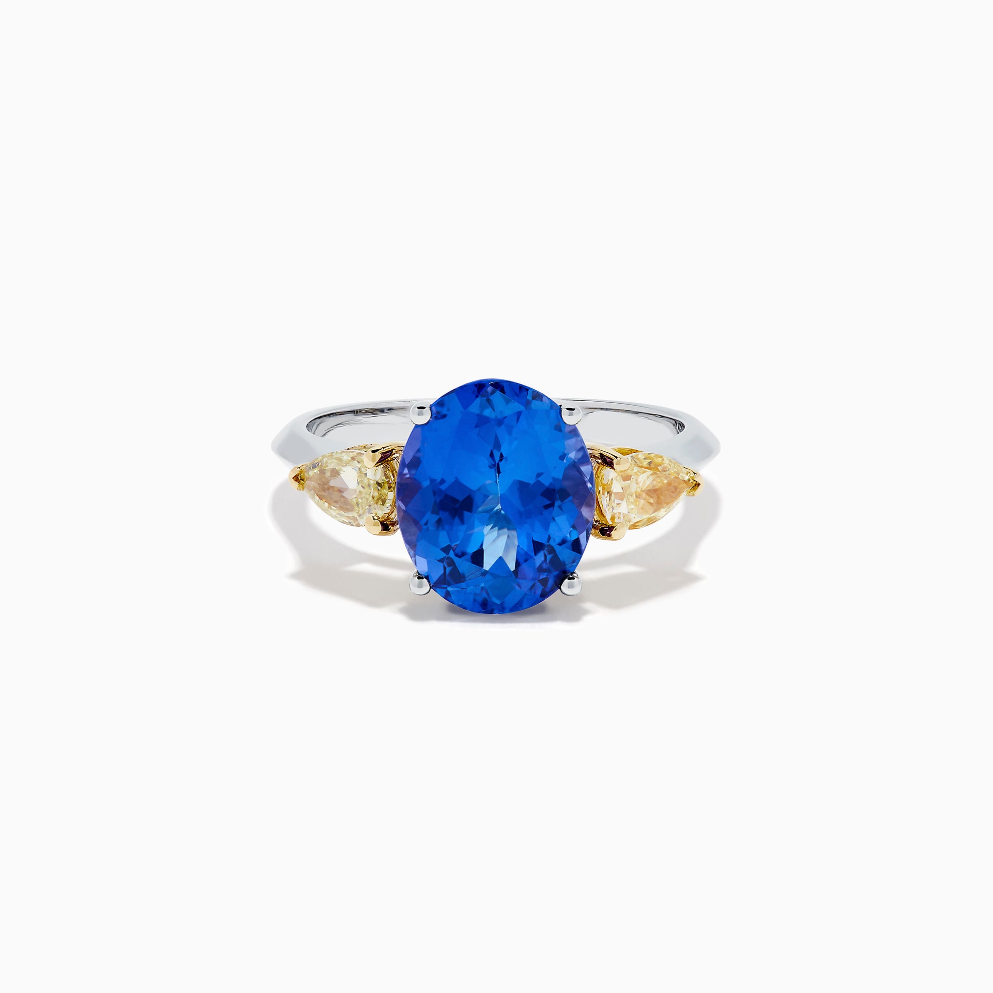 A striking 18K two tone gold ring featuring a large oval blue tanzanite center and two pear-shaped yellow diamonds on each side, displayed against a plain white background.