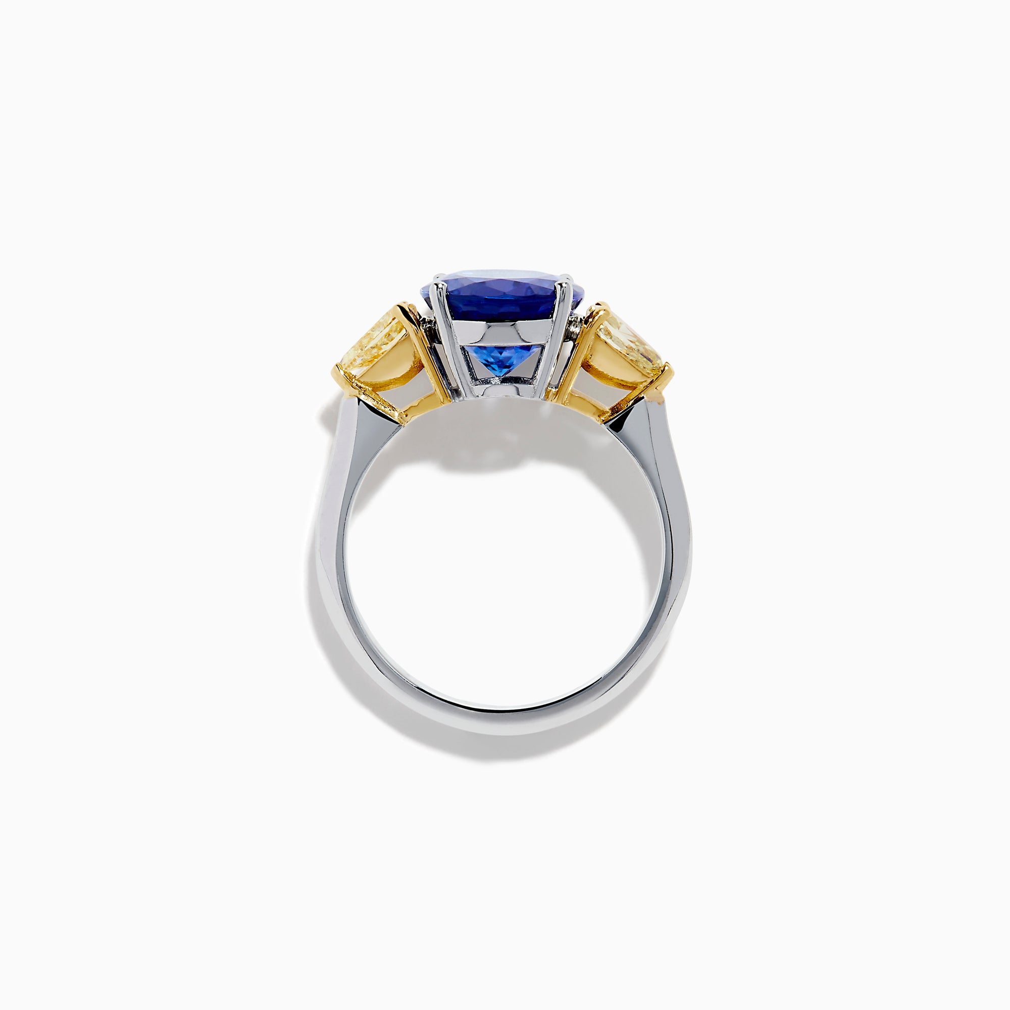A striking 18K two tone gold ring featuring a large oval blue tanzanite center and two pear-shaped yellow diamonds on each side, displayed against a plain white background.