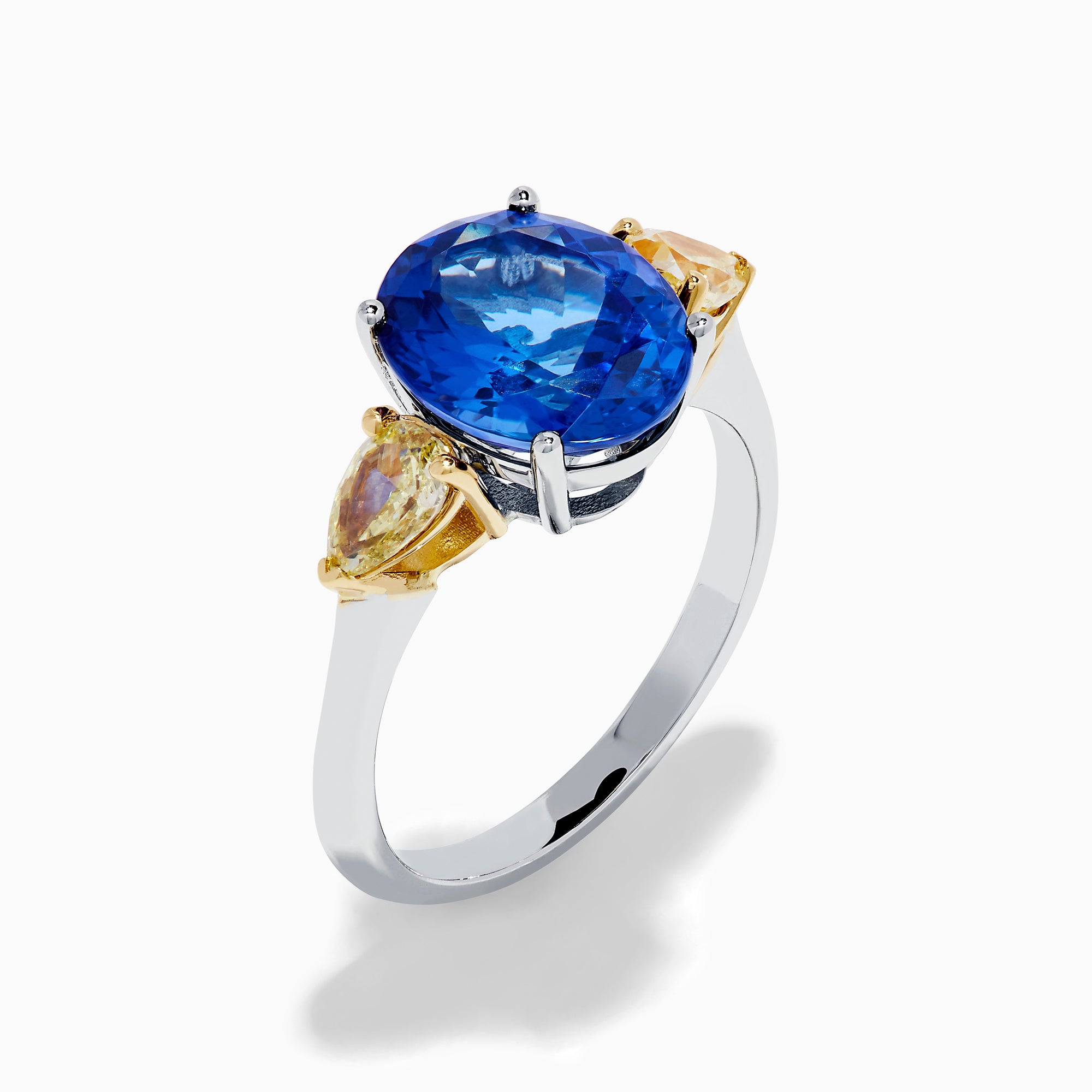 A striking 18K two tone gold ring featuring a large oval blue tanzanite center and two pear-shaped yellow diamonds on each side, displayed against a plain white background.