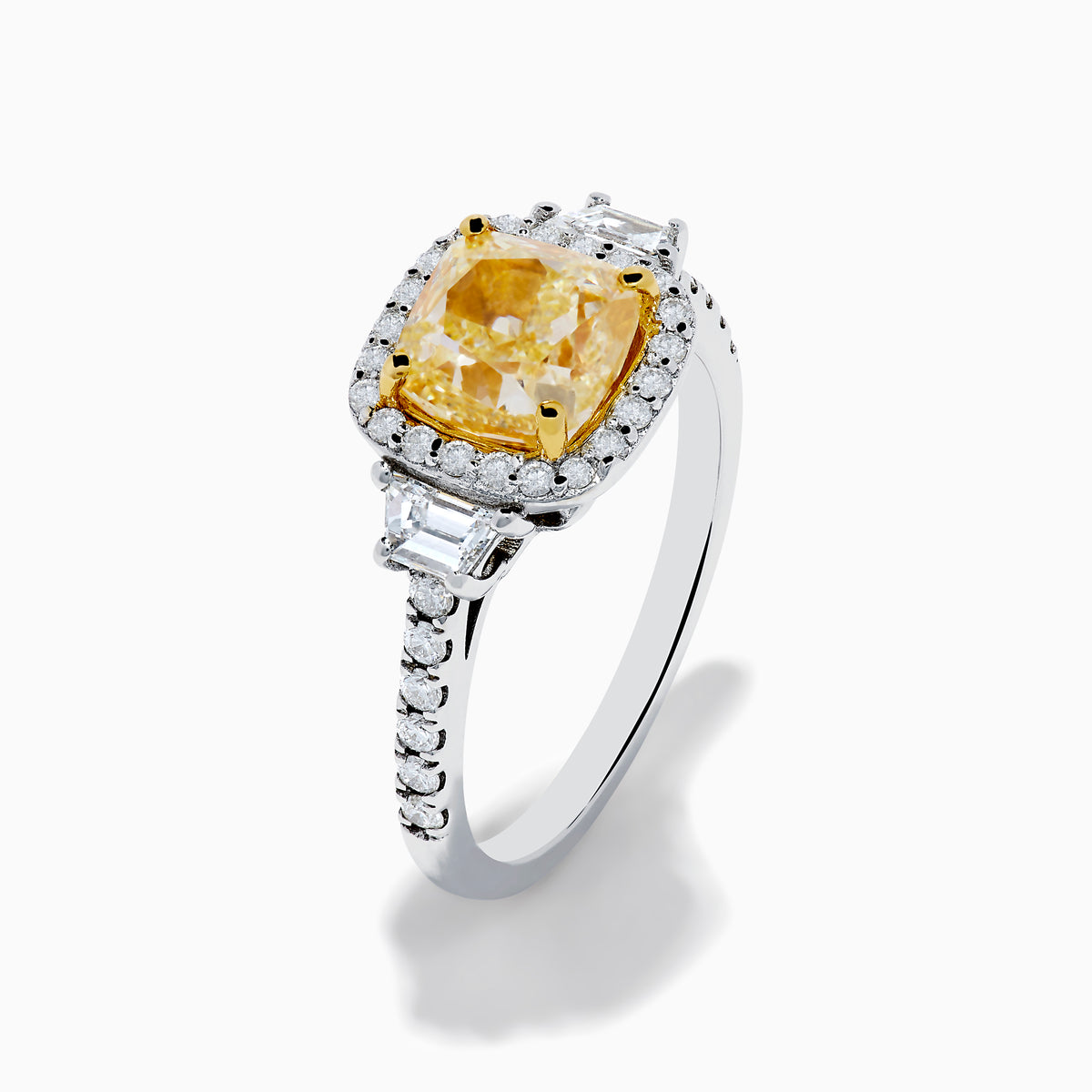 The Canare 18K Two Tone Gold White and Yellow Diamond Ring features a cushion-cut yellow diamond center, framed by a halo of white diamonds and more diamonds set along the band in elegant white gold.