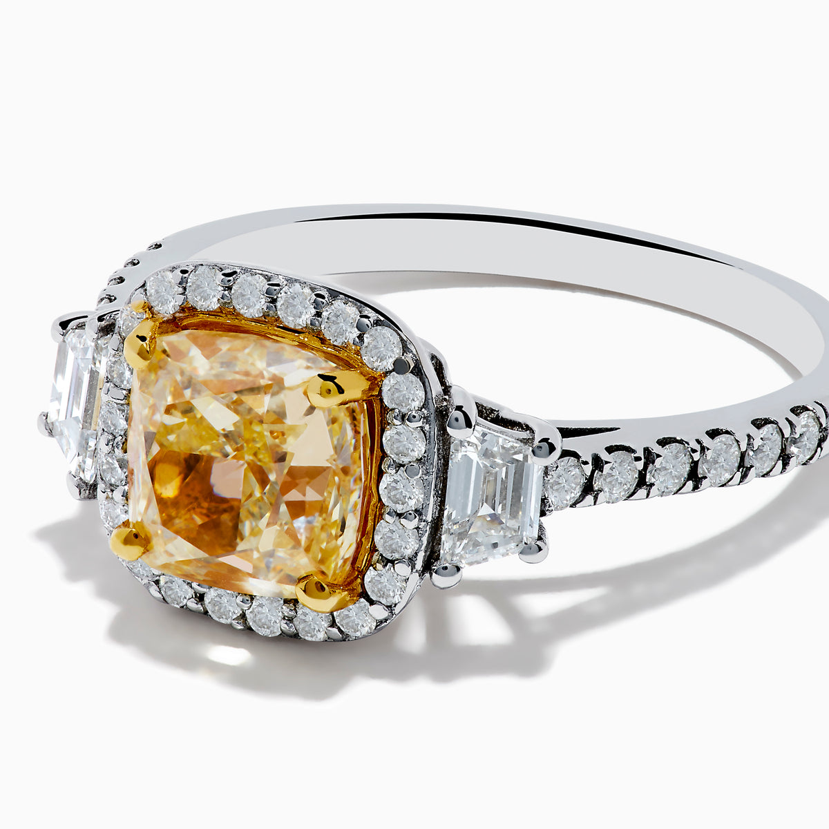 The Canare 18K Two Tone Gold White and Yellow Diamond Ring features a cushion-cut yellow diamond center, framed by a halo of white diamonds and more diamonds set along the band in elegant white gold.