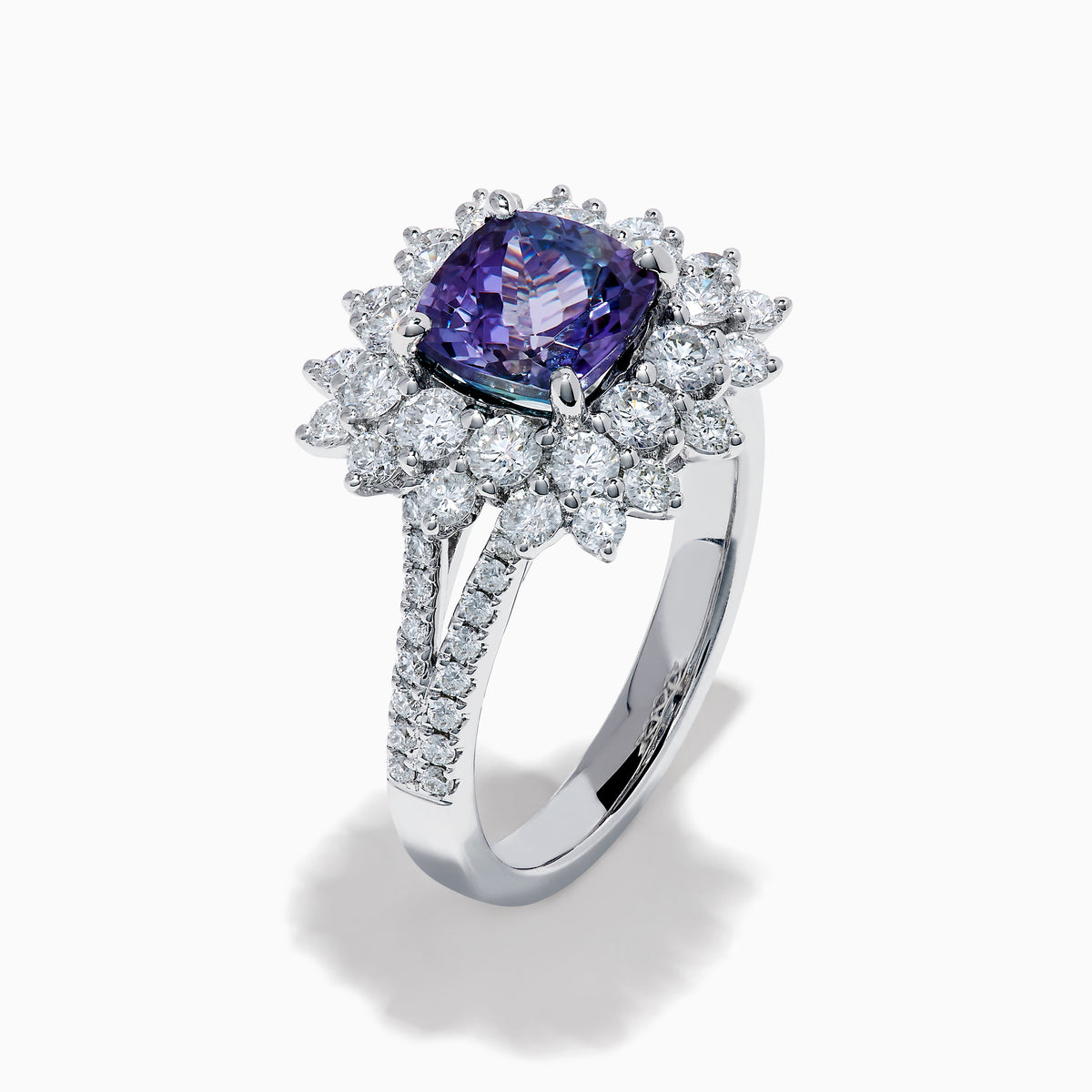 The 18K White Gold GIA Certified Zoisite and Diamond Ring features a cushion-cut blue-purple zoisite center stone with a starburst diamond halo, creating a striking look against the white gold setting.
