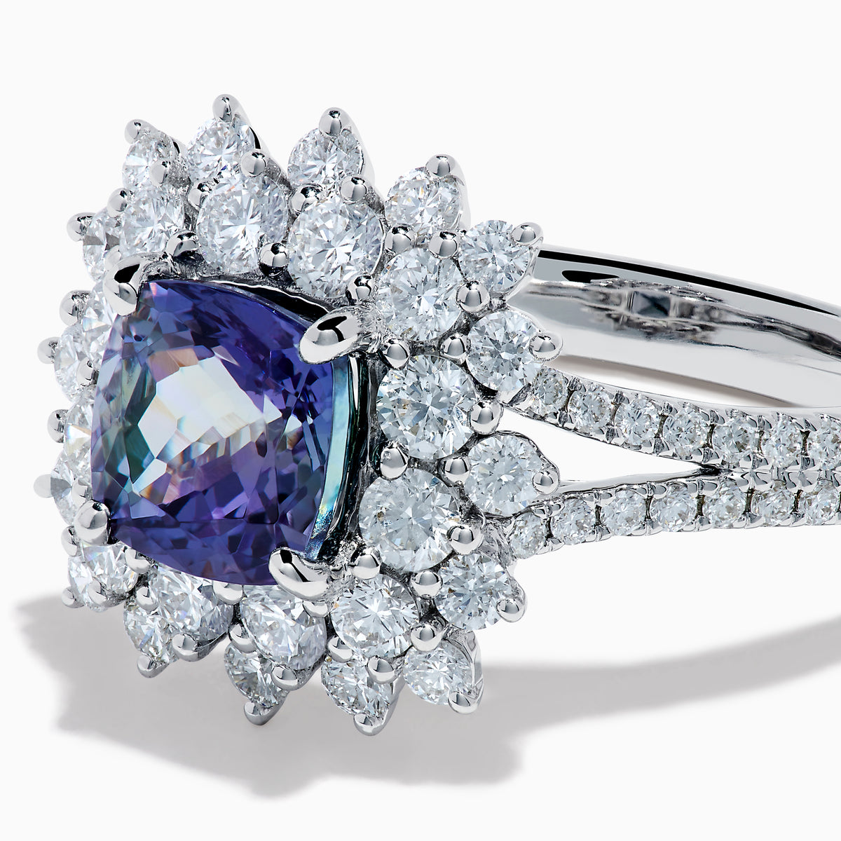 The 18K White Gold GIA Certified Zoisite and Diamond Ring features a cushion-cut blue-purple zoisite center stone with a starburst diamond halo, creating a striking look against the white gold setting.