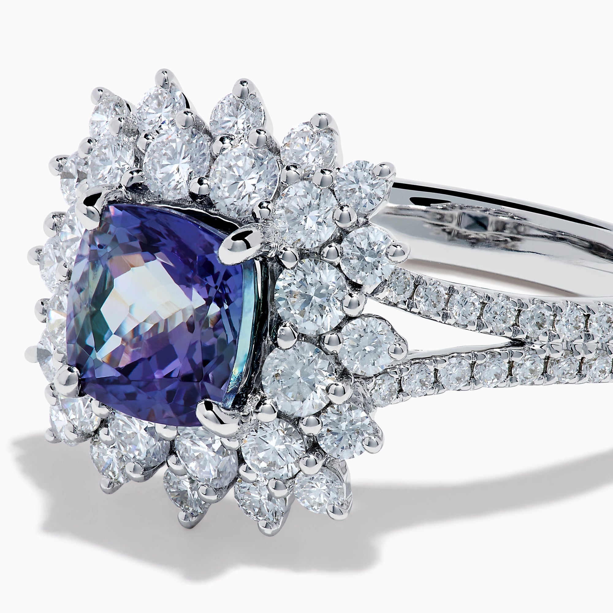 The 18K White Gold GIA Certified Zoisite and Diamond Ring features a cushion-cut blue-purple zoisite center stone with a starburst diamond halo, creating a striking look against the white gold setting.