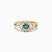 The 18K Yellow Gold Alexandrite and Diamond Swirl Halo Ring features a central oval blue alexandrite, two marquise-cut diamonds, and rows of small round diamonds in an eye-shaped swirl design.