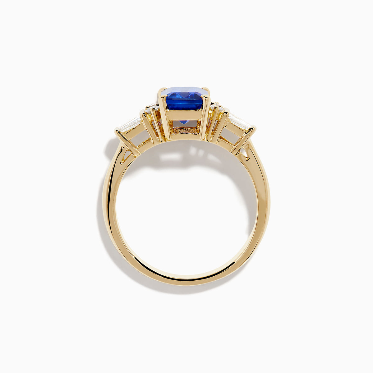 The Nahla 14K Yellow Gold Tanzanite and Diamond Ring showcases a rectangular blue tanzanite center, with two round diamonds and two baguette-cut white stones on each side, displayed on a white background.