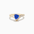 The Nahla 14K Yellow Gold Tanzanite and Diamond Ring features a triangular blue tanzanite center, accented by a curved row of sparkling round white diamonds on one side of the band.