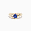 The Nahla Siri 14K Yellow Gold Tanzanite and Diamond Ring features a triangular blue tanzanite and a small round diamond, shown on a plain white background.