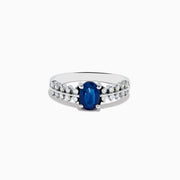 The 14K White Gold Blue Sapphire and Diamond Ring showcases an oval blue sapphire center, accented by two rows of round diamonds on each side, elegantly set against a white background.