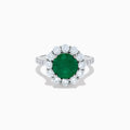 The 18K White Gold Emerald and Diamond Halo Ring features a large round green emerald center, surrounded by sparkling diamonds on the halo and band, beautifully displayed on a white background.